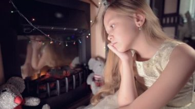 Şenlik ışıkları ve Noel ağacının arkaplanına karşı şenlikli bir elbise giymiş küçük bir kız ne yazık ki bulanıklığın içinde bir yere bakıyor ve odaklanma hareketi yapıyor. Bozuk tatil kavramı