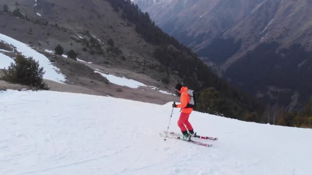 Лыжник в оранжевом костюме совершает прыжок весной, когда вечером снега немного. Концепция закрытия лыжного сезона — стоковое видео