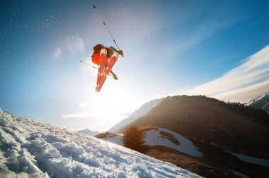 Baharda bir vurucudan atlayıp dağların ve mavi gökyüzünün arka planına atlayan bir kayakçı. Geniş açılı yakın plan. Kayak sezonunu kapatma ve baharda kayak yapma kavramı.