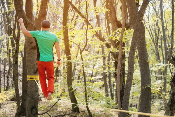 Arkadan bakan sakallı bir adam güneşli bir öğleden sonra sonbahar ormanında ip boyunca yürür. Aktif orta yaşlı insanların eğlence ve yeniden canlandırma konsepti — Stok fotoğraf
