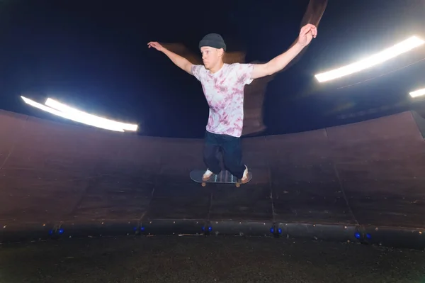 Um jovem skatista cavalga a uma velocidade lateral ao longo da rampa, estendendo as mãos para os lados. Tiro noturno com longa exposição à velocidade noturna em um parque de skate — Fotografia de Stock