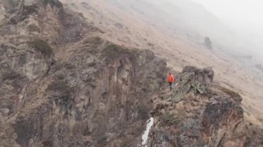 Güneş gözlüklü, şortlu ve ceketli şık bir genç adam vadi boyunca sopalarla yürüyor.