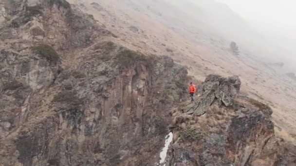 Vista aérea de um jovem elegante em um boné de óculos de sol e shorts com uma jaqueta caminha trekking com paus ao longo do desfiladeiro — Vídeo de Stock