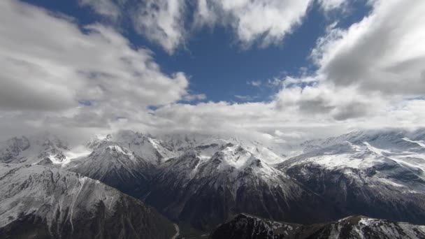 4K tijdbrede hoek hoog boven de kloof zweven snel wolken die de besneeuwde toppen van hoge bergen bedekken. Het concept van het veranderen van het weer in de bergen onder de kloof dorp — Stockvideo