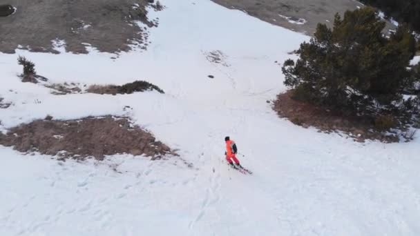 Ein luftig wirkender Skifahrer im orangefarbenen Anzug macht im Frühling einen Kickersprung, wenn abends wenig Schnee liegt. Das Konzept, die Skisaison zu beenden