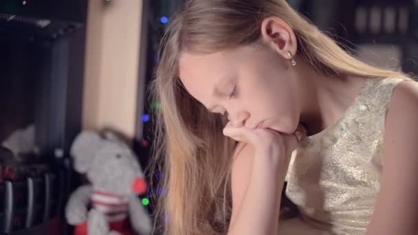 お祝いの光とクリスマスツリーを背景にお祝いのドレスの女の子は悲しいことに焦点を当てるためにぼかしや動きの下どこかを探します。甘やかされた休日の概念 — ストック動画