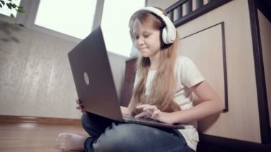 Yedi yaşında, elinde dizüstü bilgisayarla beyaz kulaklıklı akıllı bir kız odasında yere bastırıyor. İnternet ve bilişim teknolojisindeki genç nesil.