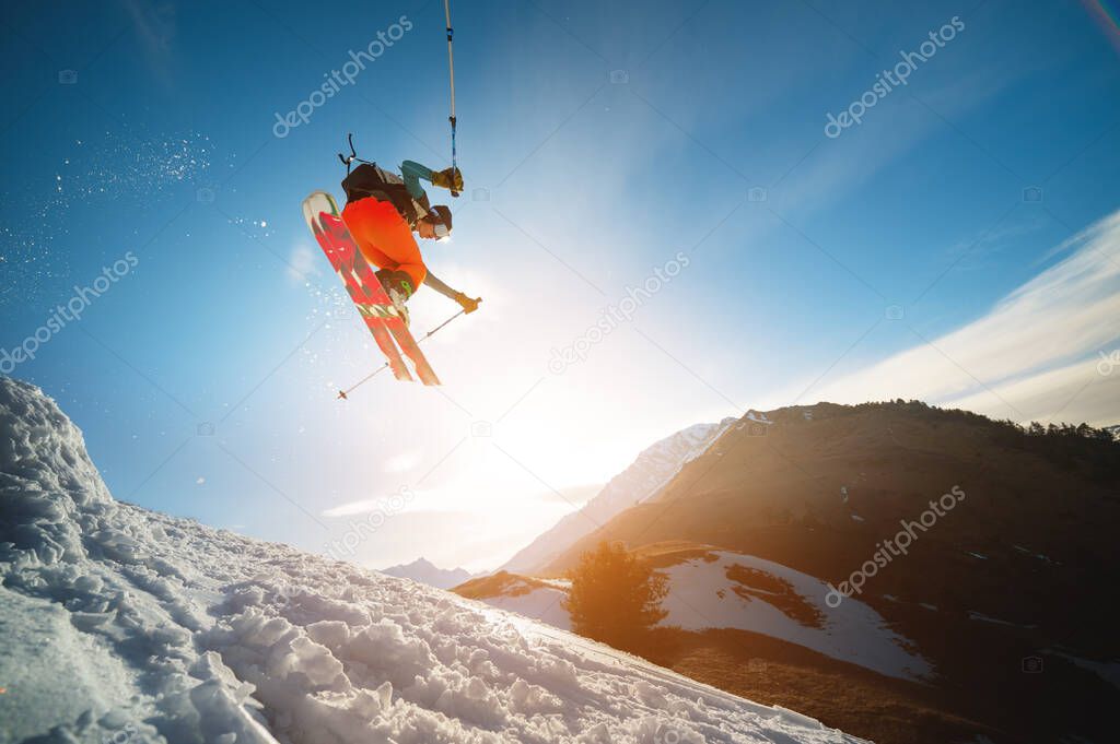 man skier in flight after jumping from a kicker in the spring against the backdrop of mountains and blue sky. Close-up wide angle.