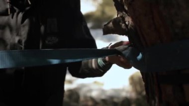 Halat ipi. Genç bir adam denge sağlamak için ağaca ip takıyor. Alanın küçük derinliğine yakın çekim