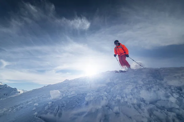 Atleta masculino esquiador salta de uma encosta coberta de neve contra o pano de fundo de uma paisagem montanhosa de montanhas cobertas de neve em um dia ensolarado. O conceito de esportes de inverno grande ângulo — Fotografia de Stock