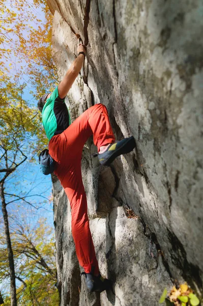 A bearded man aged with a bag of magnesia and rock shoes is trainered on a not high rock in the woods. Training of climbers in natural conditions