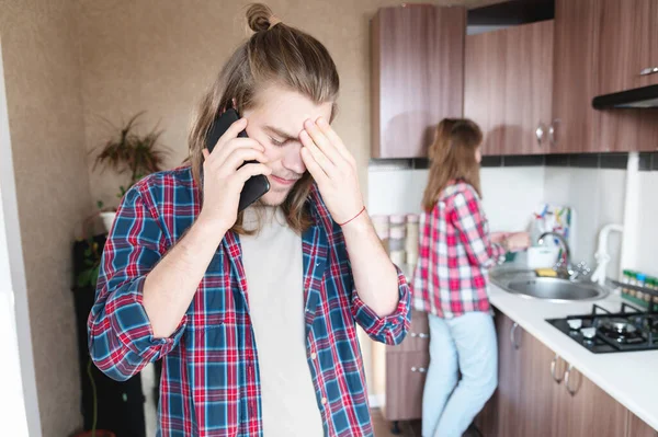 Alteración grave joven de pelo largo de pie en la cocina utiliza su teléfono móvil o pedir un servicio de Internet hablando por teléfono — Foto de Stock