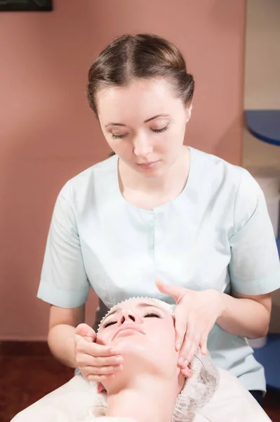 Una masajista profesional le hace un masaje facial a un cliente en un salón de cuidado facial de spa. El concepto de masaje facial y cuidado de la piel —  Fotos de Stock