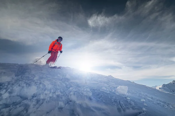 Atleet mannelijke skiër springt van een besneeuwde helling tegen de achtergrond van een berglandschap van besneeuwde bergen op een zonnige dag. Het concept van de wintersport groothoek — Stockfoto