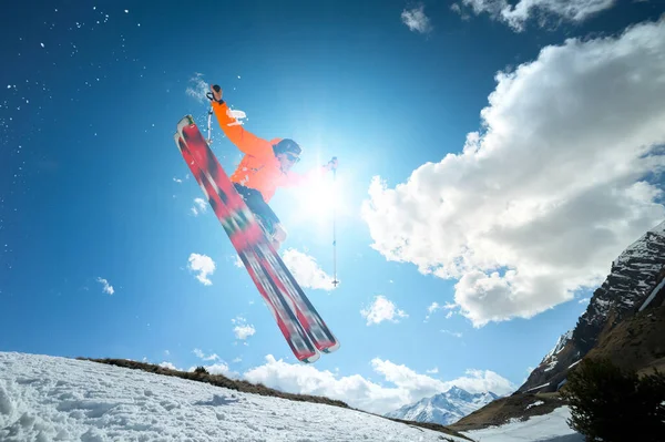 Ein junger, stylischer Mann mit Sonnenbrille und Schirmmütze zeigt einen Trick, als er an einem sonnigen Tag mit einem Schneeschuh gegen den blauen Himmel und die Sonne springt. Das Konzept des Park-Skifahrens im Winter oder Frühling — Stockfoto