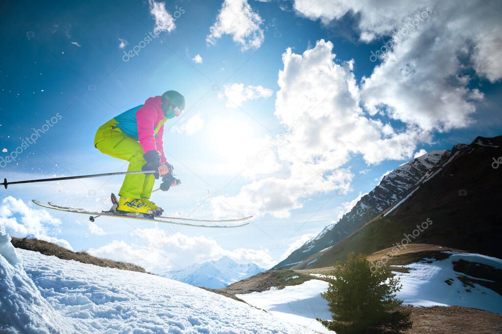 Girl skier in flight after jumping from a kicker in the spring against the backdrop of mountains and blue sky. Close-up wide angle. The concept of closing the ski season and skiing in spring
