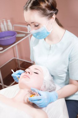 Güzellik muayenehanesi kadın güzellik uzmanı çekici bir müşterinin yüzüne fırça tazeleyici maske takıyor. Profesyonel kozmetik hizmetleri