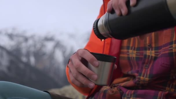 Зблизька людина виливає гарячий чай з термоса в кухню проти засніжених гір Кавказу. Поняття теплоти і потіхи в подорожах.. — стокове відео