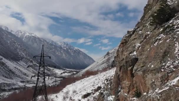 Volo panoramico aereo in una gola di montagna vicino alle scogliere nel pomeriggio. Avvicinamento al supporto della linea di trasmissione elettrica ad alta tensione. — Video Stock