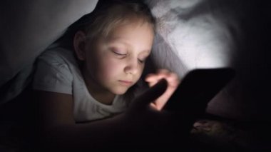 Keskin bir küçük kız gece battaniyenin altında akıllı bir telefonla oynar. Çocuklar mobil cihazlarla gerçeklikten ayrılıyorlar. Çocuk gizli telefon kullanıyor