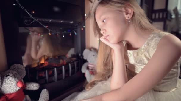 Mała dziewczynka w świątecznej sukience na tle świątecznych świateł i choinki niestety patrzy gdzieś w dół rozmycia i ruchu, aby skupić. Koncepcja zepsutego urlopu — Wideo stockowe