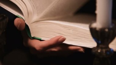 Yakından, kitap sayfalarını karıştıran beyaz bir kız. Mumlar yanıyor. Cadılar Bayramı konsepti. Sığ alan derinliği