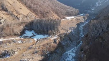 Çamur kaymaları ve çığ yüzünden hava manzaralı beton koruyucu yapılar. Kısmen yok edilmiş koruyucu yapı. Turuncu ceketli adam ayağa kalkar ve sigortasız yüksekliğe bakar.