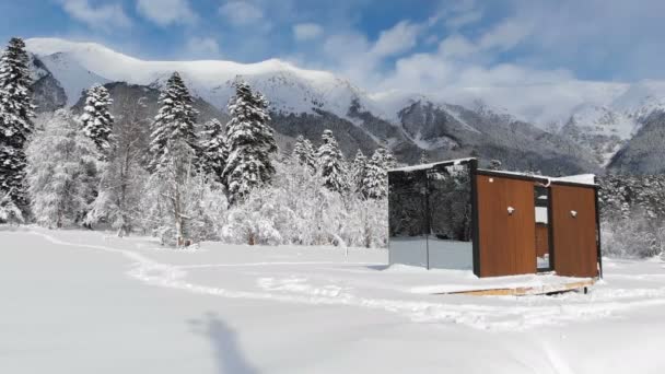 Вид з повітря на інноваційний високотехнологічний будинок з дзеркальними стінами серед зимового лісу в горах. Концепція екологічного туризму в горах. Сучасна архітектура в заповідниках — стокове відео