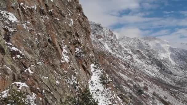 Aerial view of the close span of the camera next to a rock wall high in the mountains in early spring green grass and snow on the slopes of the mountains — Stock Video