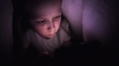 Keskin bir küçük kız gece battaniyenin altında akıllı bir telefonla oynar. Çocuklar mobil cihazlarla gerçeklikten ayrılıyorlar. Çocuk gizli telefon kullanıyor