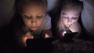 İki hevesli küçük kız gece bir battaniyenin altında akıllı telefonda oynuyorlar. Çocuklar mobil cihazlarla gerçeklikten ayrılıyorlar. Çocuk gizli telefon kullanıyor