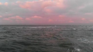 Akşam günbatımından hemen sonra Baltık Denizi kıyı şeridi üzerindeki uçuşun havadan görüntüsü. Gökyüzündeki kuş bakışı pembe bulutlardan denizin arka planına ait bir video kavramı