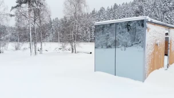 Vista aérea de uma inovadora casa de alta tecnologia com paredes transparentes espelhadas no inverno perto de uma floresta de coníferas nas montanhas do Cáucaso ou dos Alpes . — Vídeo de Stock