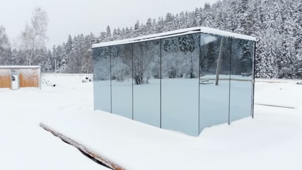 Flygfoto av ett innovativt högteknologiskt hus med speglade transparenta väggar på vintern nära en barrskog i bergen i Kaukasus eller Alperna. — Stockvideo