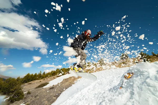 Stylowa młoda dziewczyna snowboardzista robi sztuczkę w skoki z kopacza śniegu przeciwko błękitne niebo chmury i góry wiosną. — Zdjęcie stockowe