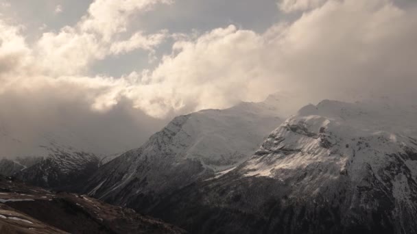 Včasné mraky proudí v horách a přelévají se přes vrcholy ve večerních horách s vysokými sněhovými čepicemi. — Stock video