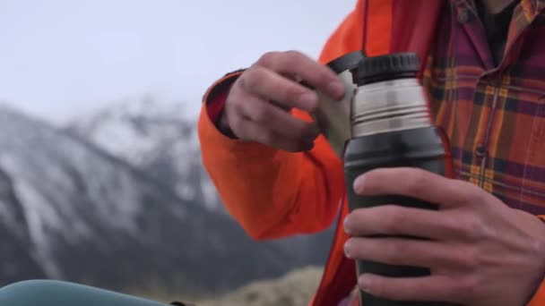 Un hombre de cerca vierte té caliente de un termo en una taza contra las montañas nevadas del Cáucaso. El concepto de calidez y confort en los viajes . — Vídeos de Stock