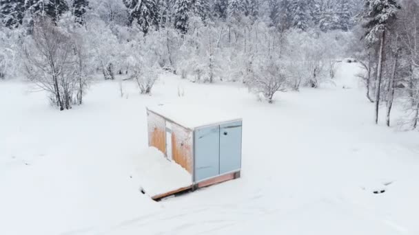 Vista aérea de una innovadora casa de alta tecnología con paredes transparentes espejadas en invierno cerca de un bosque de coníferas en las montañas del Cáucaso o los Alpes. — Vídeo de stock