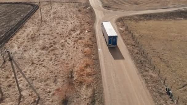 Vista aérea de un camión grande con un remolque que conduce a lo largo de un camino de tierra en busca de un lugar para un giro en U en las inmediaciones de una carretera suburbana. — Vídeo de stock