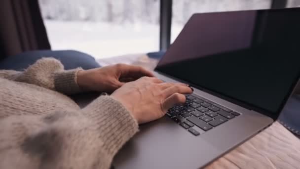 Nahaufnahme des Mädchens Hände drucken etwas auf dem Laptop sitzt auf einem Bett mit einem Laptop in den Händen gegen die Panoramafenster, hinter denen der Winterwald im Schnee. — Stockvideo