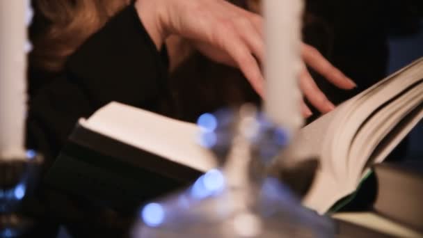 Primo piano attraente ragazza caucasica sfogliando un libro. Le candele stanno bruciando. Concetto di festa di Halloween. Profondità di campo ridotta — Video Stock