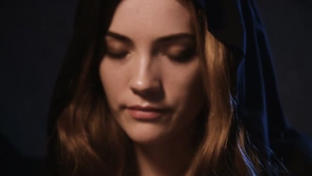 Un portrait en gros plan d'une jolie femme blanche dans une capuche noire aux cheveux blonds jouant le look enchanteur et flirtant. Le concept de la magie de l'amour et la fête d'Halloween