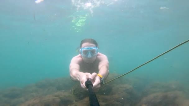 Un selfie disparado bajo el agua por un hombre caucásico luciendo un físico flota maravillosamente bajo el agua. El concepto de buceo libre y recreación en la costa del mar o en el océano — Vídeo de stock