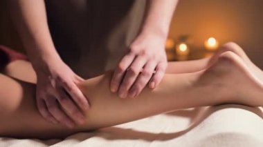 Baldır kasının el masajına yakın çekim. Profesyonel bir masaj terapisti bir kadının bacağına güzel bir ışıkla masaj yapar.