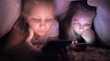 İki hevesli küçük kız gece bir battaniyenin altında akıllı telefonda oynuyorlar. Çocuklar mobil cihazlarla gerçeklikten ayrılıyorlar. Çocuk gizli telefon kullanıyor