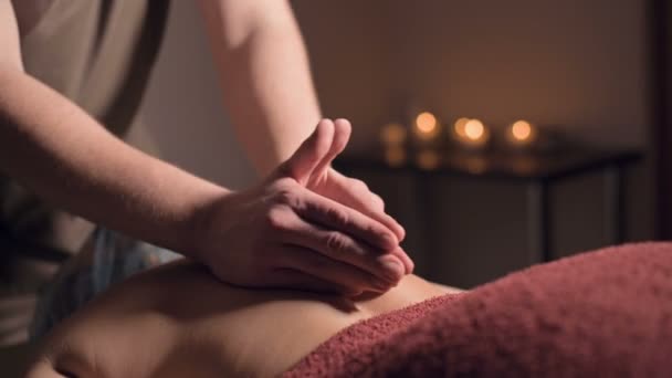 Un jeune masseur fait une cliente de massage professionnelle dans un salon de massage professionnel avec des bougies allumées dans une pièce sombre — Video