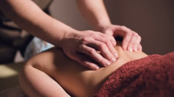 Un joven masajista masculino hace un masaje profesional cliente chica en un salón de masajes profesional con velas encendidas en una habitación oscura — Vídeo de stock