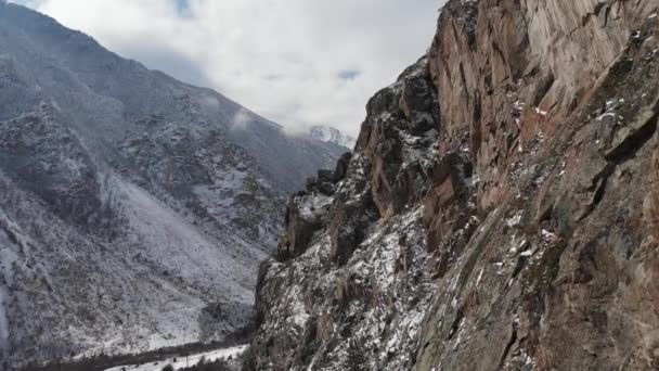 Luftaufnahme einer engen Spannweite neben den Felsen in den Bergen durch die Schlucht, unter der die Asphaltstraße verläuft — Stockvideo