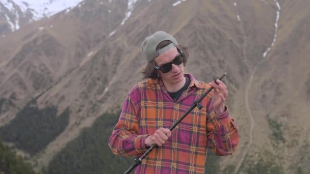 Un gros plan d'un jeune homme dans les montagnes prépare des bâtons de trekking pour une promenade scandinave avant utilisation. Le concept de trekking et de préparation au tourisme — Video