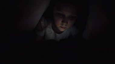 Keskin bir küçük kız gece battaniyenin altında akıllı bir telefonla oynar. Çocuklar mobil cihazlarla gerçeklikten ayrılıyorlar. Çocuk gizli telefon kullanıyor